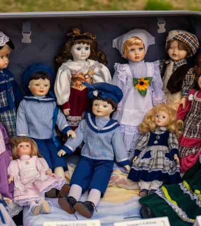 A veritable crowd of elegantly-dressed dolls sit and stand in a suitcase