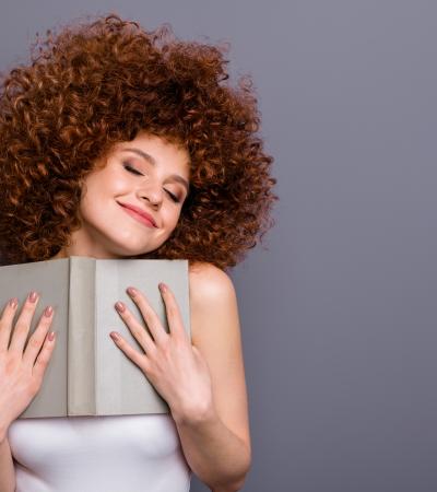 college age girl with wild curly red hair embraces a favorite book with ecstatic facial expression
