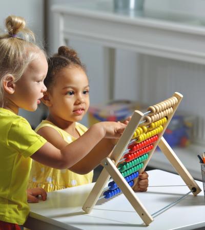 preschool girls of different ethnicities sit together at table counting on abacus