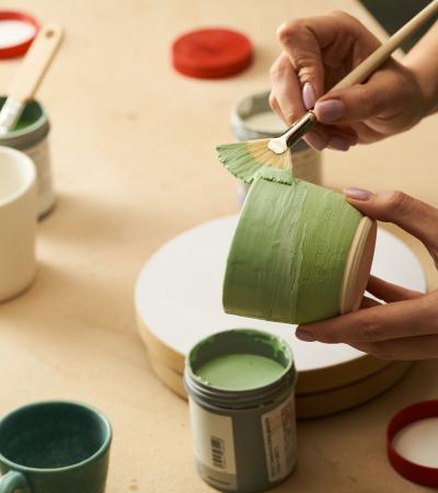 Close-up of painting clay mug with green paint