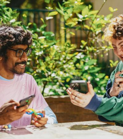 Two people holding mobile phones and tangle fidgets smile as they share a phone screen.