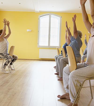 Group of senior citizen women do chair yoga.