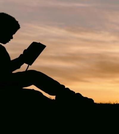 Photo of a silhouetted child reading.