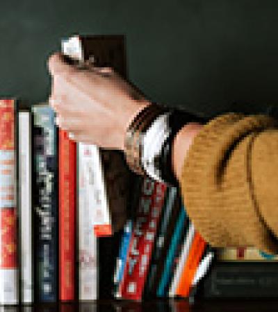 Hand selecting a book from several on a shelf