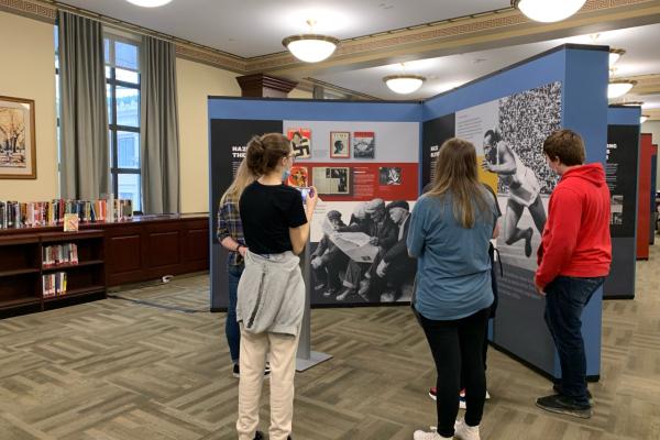 Photograph of a group of people looking at the Americans and the Holocaust exhibition panel inside of Penn State library.