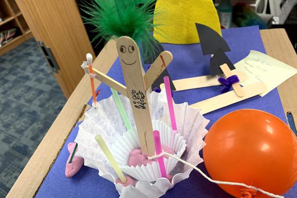 A human figure made out of popsicle sticks with clay and a balloon