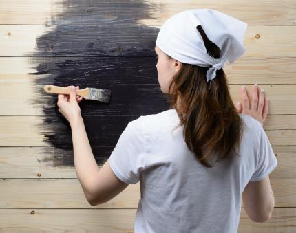 Teenage girl wearing white shirt and headscarf paints wooden wall black