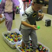 Children dressed as superheroes walk through tubs filled with Legos