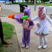 Children dressed as superheroes shoot squirt guns at a target.