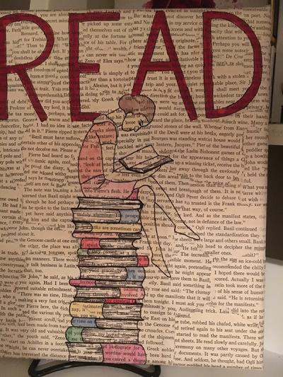 A page from a book with the word "read" drawn on it in red marker with a drawing of a girl sitting on a stack of books.