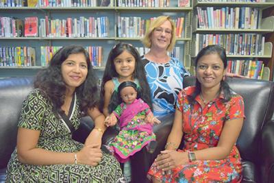 Three adult women and a child sit on a couch, smiling, the child is holding a doll.