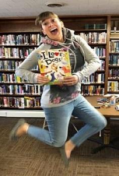 Chelsea Price jumps while holding a book called "I Love Dogs"