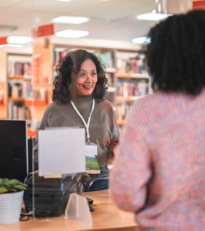 Librarian serving a patron behind the circulation desk in a library. 