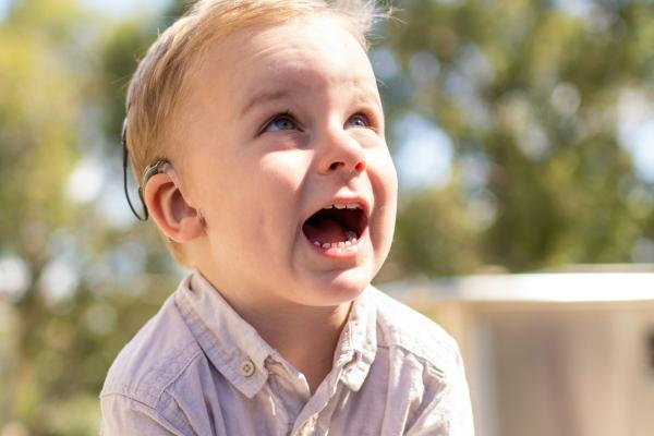 Photograph of a toddler with a hearing aid smiling up.