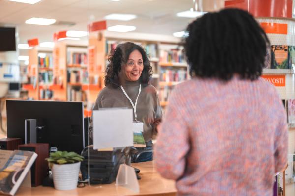 Librarian serving a patron behind the circulation desk in a library.