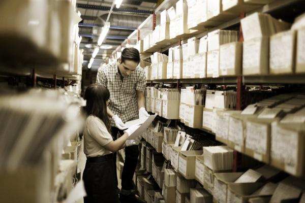 Photograph of two people looking through boxes of archived materials on bookshelves.