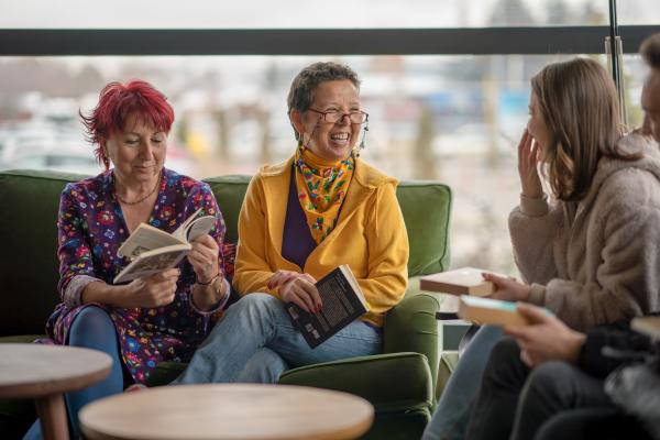 Photograph of a group of three people smiling with books open, sitting around a table.