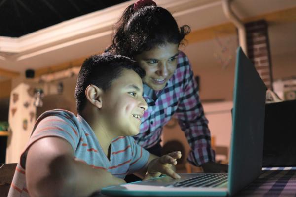Photograph of smiling child working on a laptop with an adult helping.