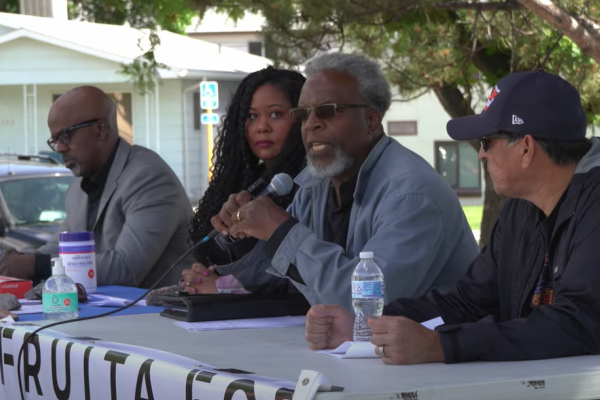 Four panelists sitting at an outdoor table participating in a conversation. One person is speaking into a microphone.